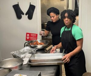 Larvita (in the rear) and one of her daughters at work in her restaurant, where she has received harassment and fines for refusing to close her business.